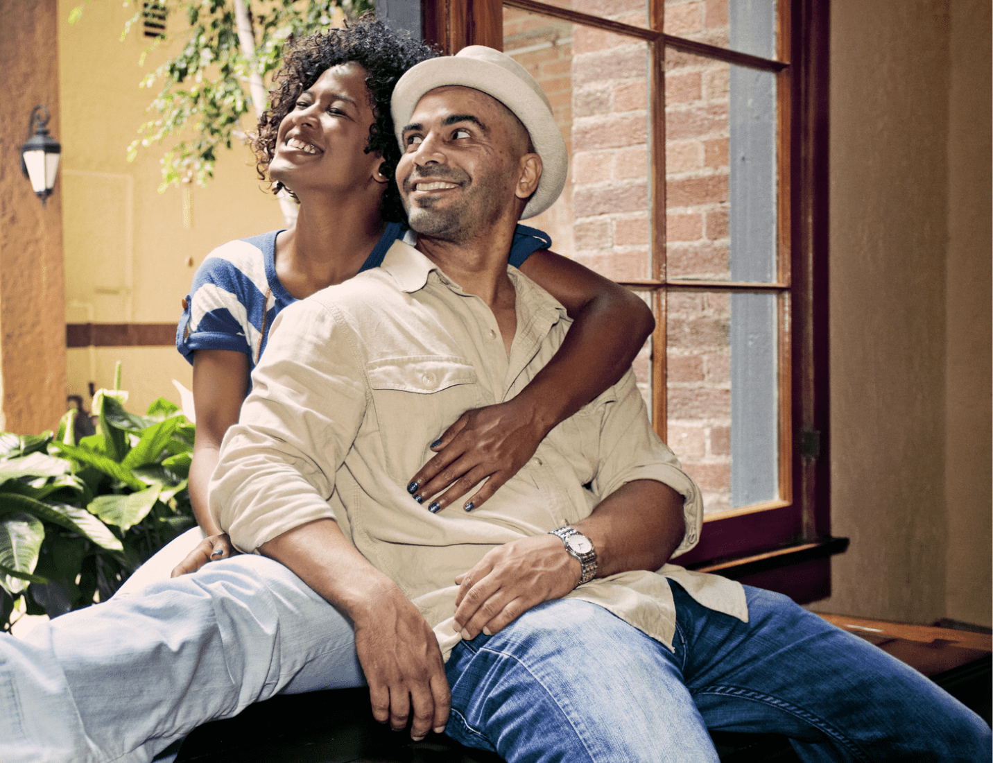 A couple sitting at a windowsill, embracing as they admire a sunny day.