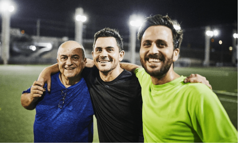 Two men smile and hug their father after playing soccer.